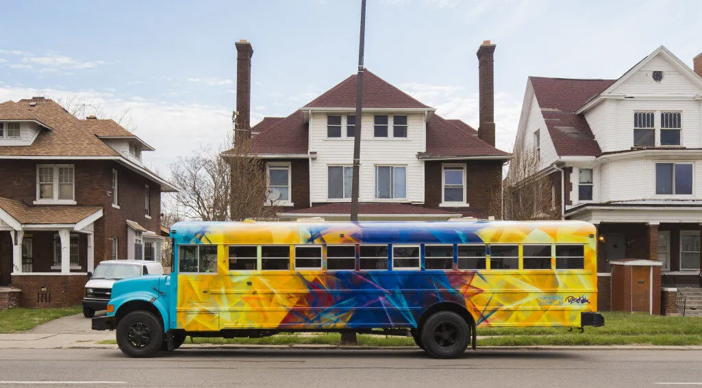 A hand-painted Detroit Bus Company bus rolling through a Detroit neighborhood