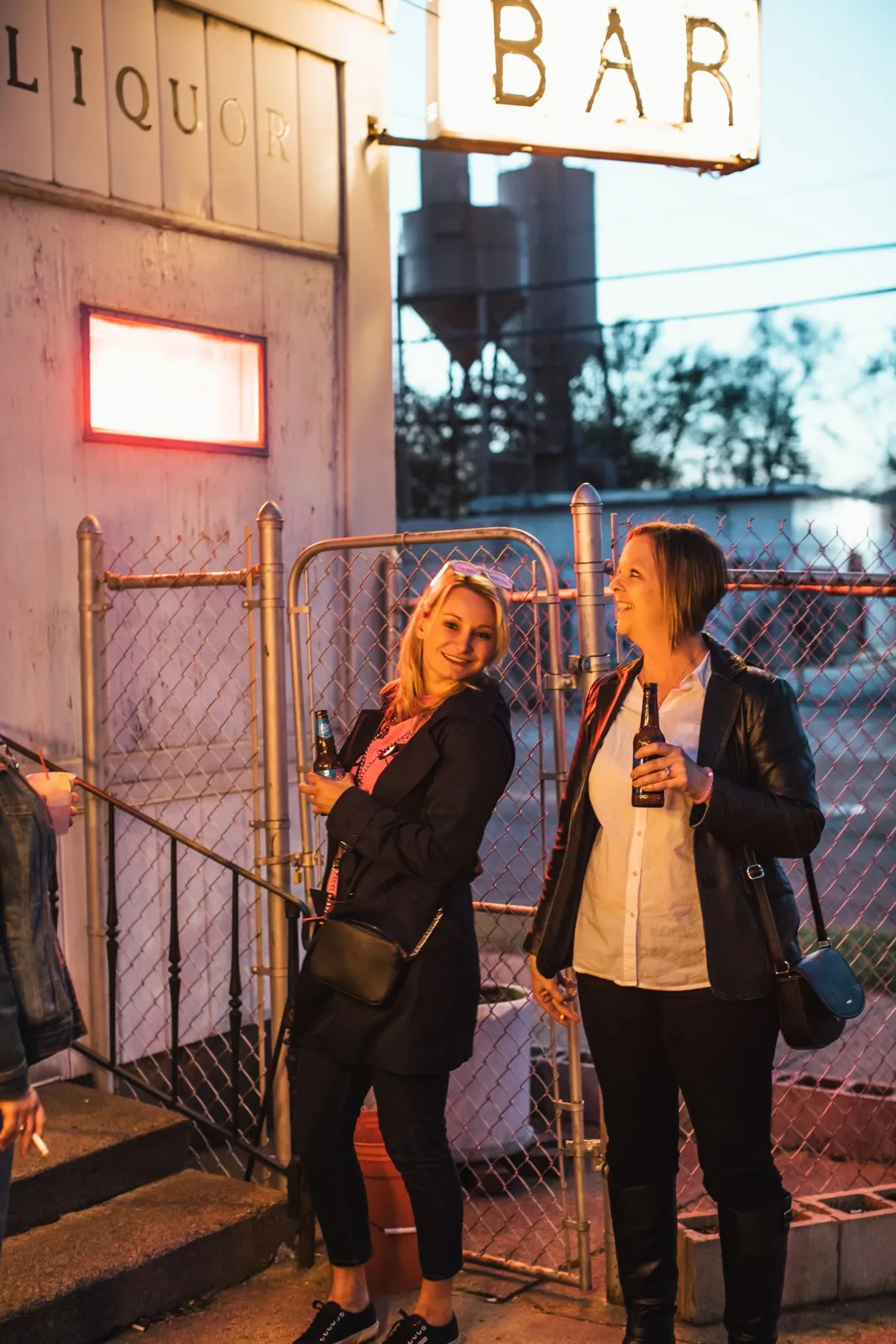 Two guests talking under a vintage neon BAR sign at dusk