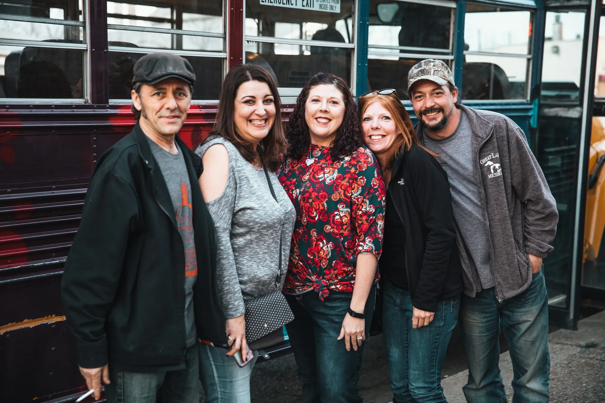 Five friends smiling in front of two hand-painted Art Buses before a bar crawl