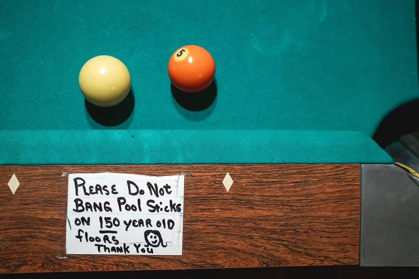 A handwritten bar sign reading 'Please do not bang pool sticks on 150 year old floors'