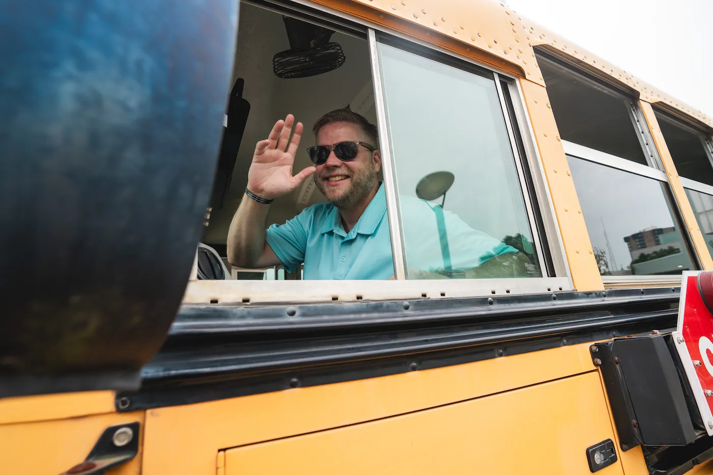 A smiling DBC driver waving from the door of a hand-painted bus