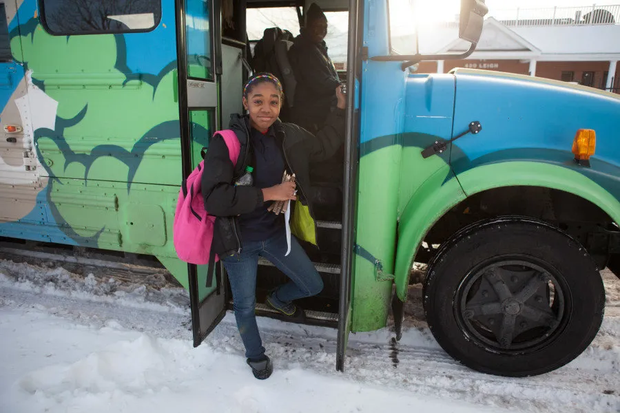 A student with a pink backpack stepping off a hand-painted bus in the snow