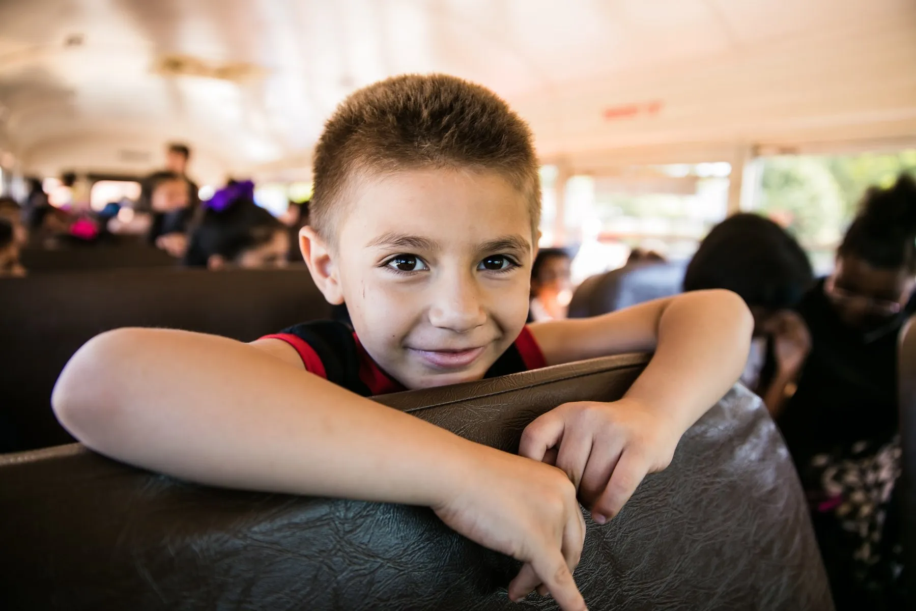 A kid grinning over the seatback of a packed, happy bus