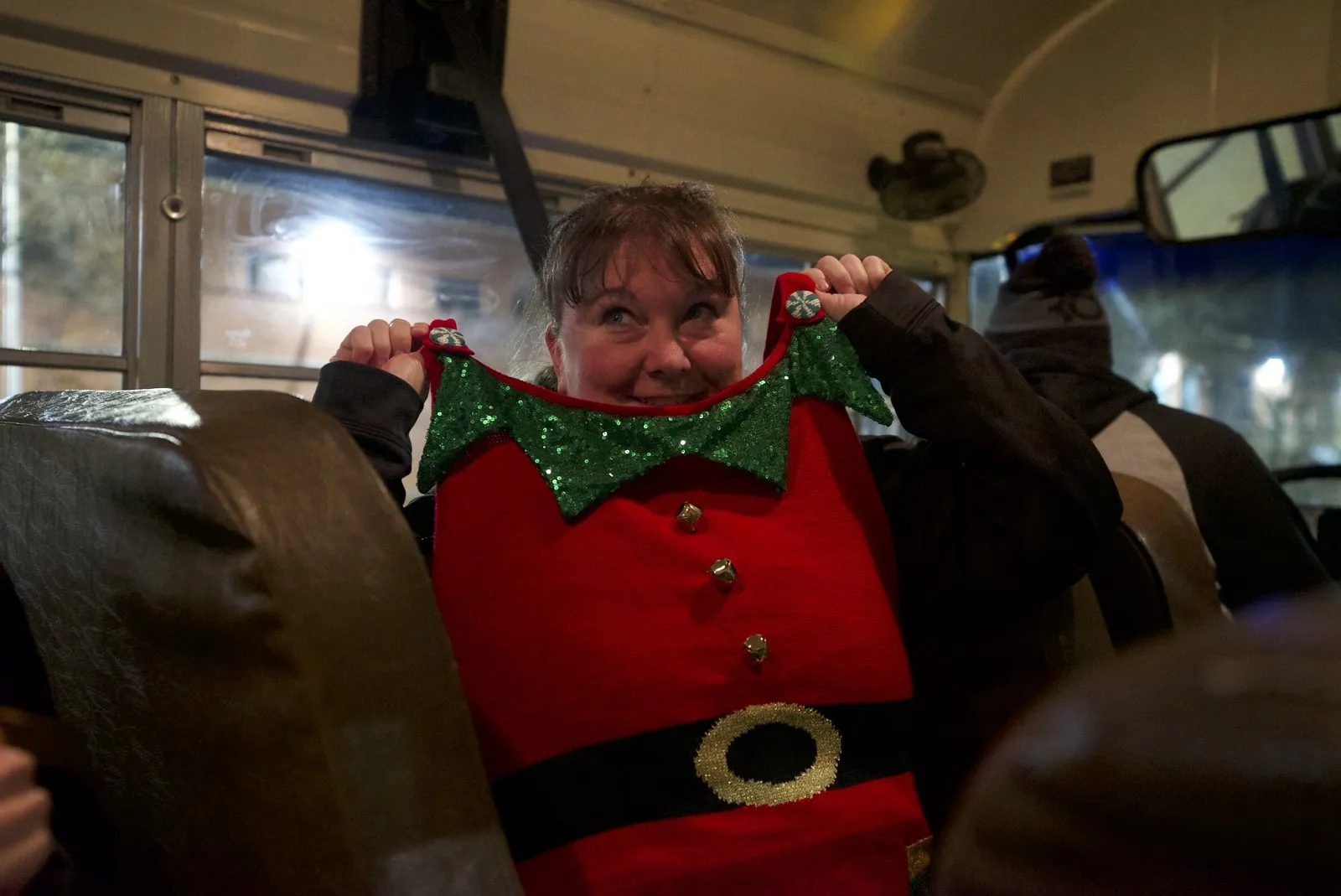 A guest peeking over a bus seat holding a tiny elf costume