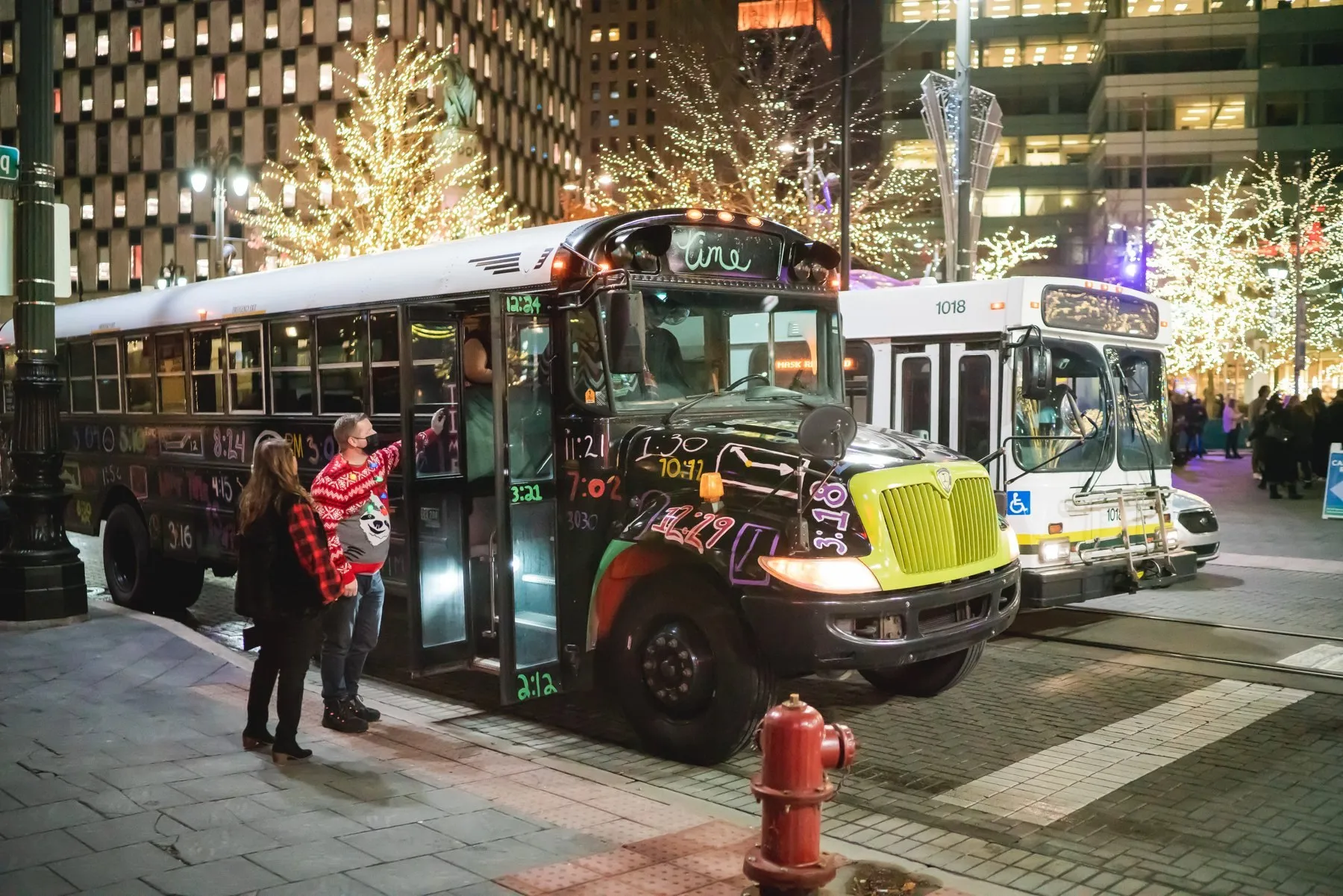 Two Detroit Bus Company buses parked under lit trees downtown