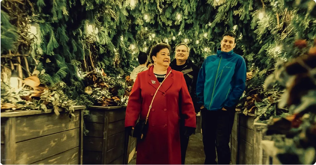 A family smiling under strings of holiday lights on the Merry & Bright tour