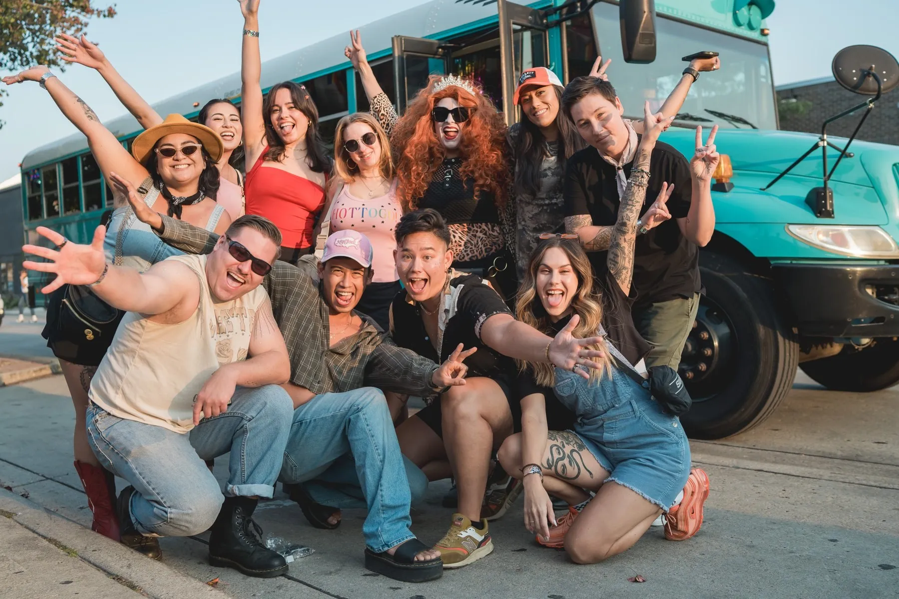 A big festival crew posing with the teal Art Bus at golden hour