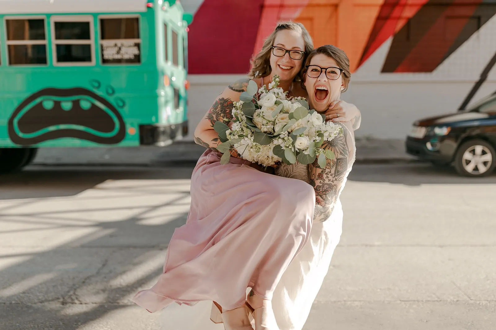 A newlywed sweeping their partner off their feet in front of the teal Art Bus