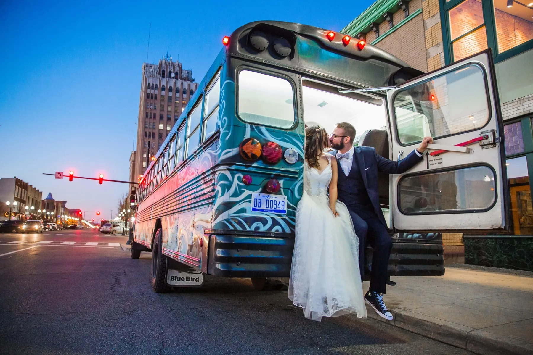A couple beside the painted bus at dusk with downtown lights behind
