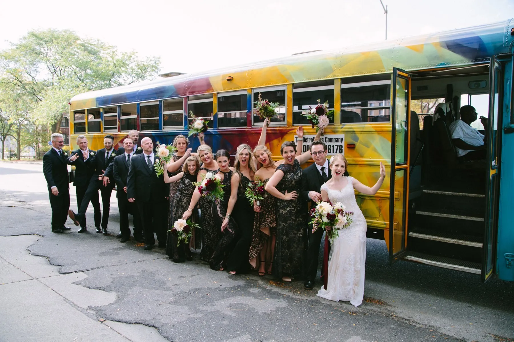 A full wedding party lined up along a rainbow-painted Art Bus downtown